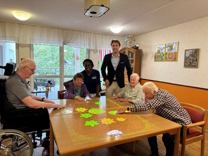 Vier Bewohnerinnen und Bewohner des AWO-Seniorenzentrums Rheinaue sitzen an der neuen Tovertafel. Daneben stehen eine Pflegekraft sowie Einrichtungsleiter Marvin Winnes.