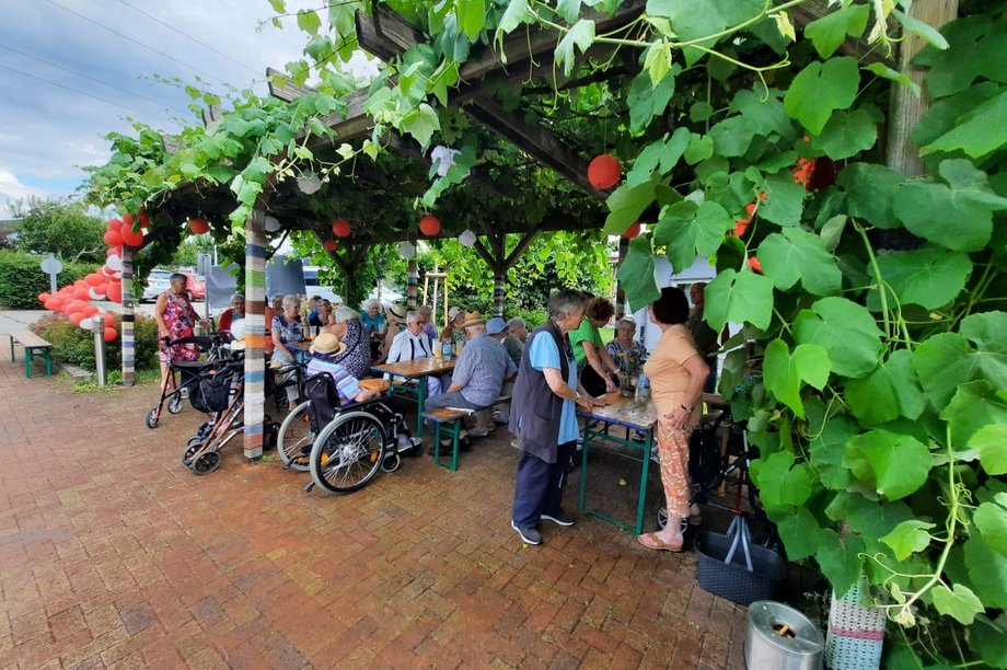 mehrere Menschen sitzen unter einem mit Pflanzen bedeckten Pavillion, der mit Lampions und Luftballonsgeschmückt ist und feiern das 25-jährige Jubiläum im AWO Seniorenzentrum Rheinaue