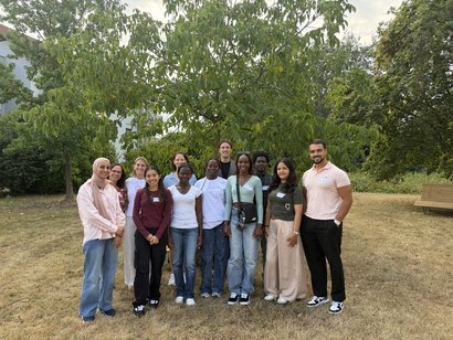 Gruppenfoto neuer Auszubildender und Mitarbeitender im Freien auf einer Wiese vor Bäumen. Die Gruppe steht für ein Willkommensfoto zusammen.