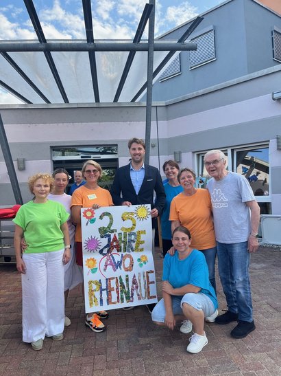 Bewohner und Bewohnerinnen sowie das Pflegepersonal halten ein Schild mit 25 Jahre AWO Seniorenzentrum Rheinaue in die Höhe